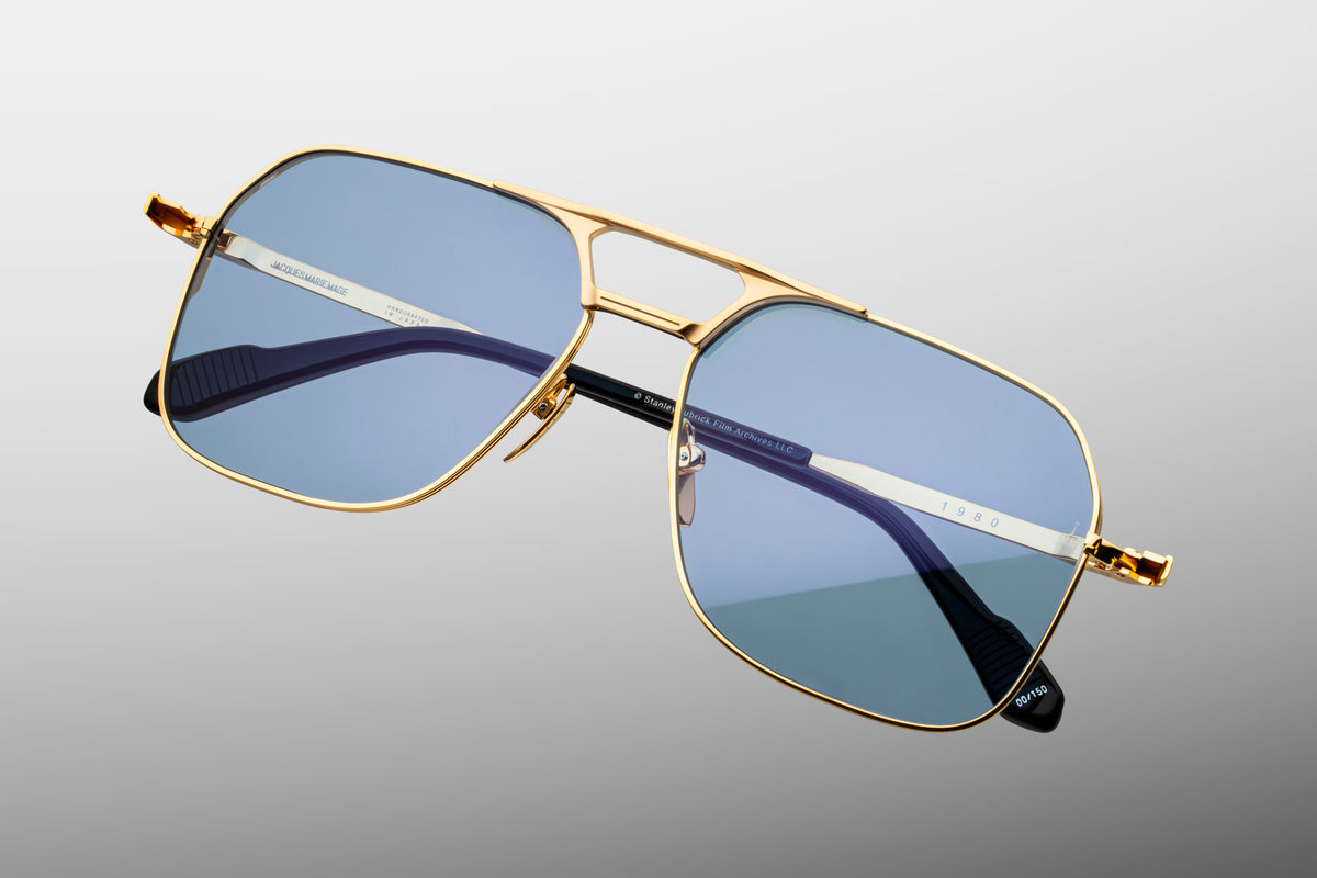 Top-down angle of the Stanley Kubrick 1980 Ciel frame. Highlights the delicate 4mm wire rims, the exact parallel spacing of the dual gold titanium bridge, the gleam of the polished luster gold nose pads, and the slight inward curvature of the long temples. WINK Optometrists