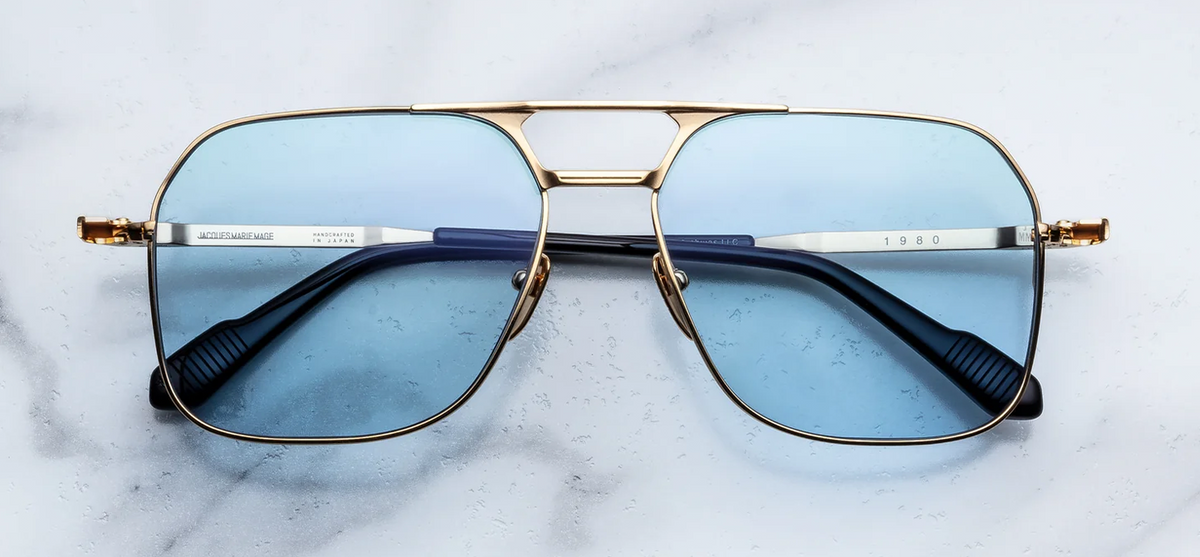 Front view of Jacques Marie Mage Stanley Kubrick 1980 sunglasses in Ciel. Features an oversized, lightweight aviator frame made of 100% beta titanium finished in brilliant moon gold. Includes a distinctive double nose bridge accented with fine black epoxy lines and fitted with striking, light-filled serene blue Armorlite lenses. WINK Optometrists