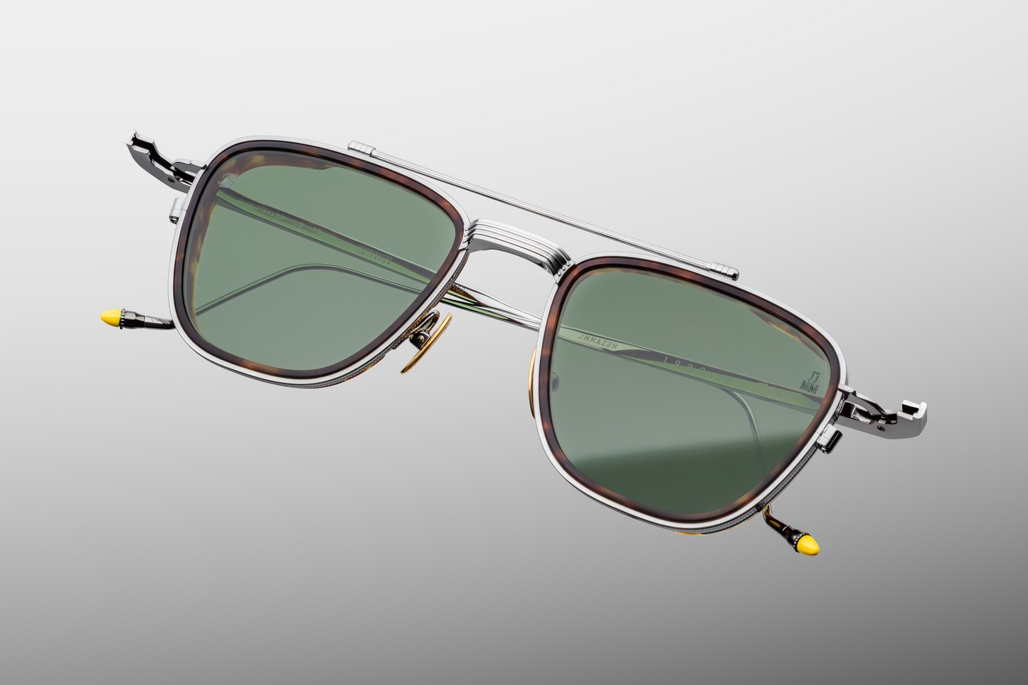 Close-up of front of Jacques Marie Mage 1992 Antique Silver sunglasses highlighting the distinctive top-bar, coined-edge eyerims, polished nose pads and Taiga green crown-mineral lenses, available at WINK Optometrists
