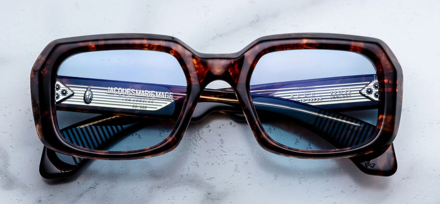 Front view of Jacques Marie Mage Aldo sunglasses in Argyle Havana tortoise shell acetate, showcasing a sculptural, oversized 1970s-style frame with deep powder blue lenses and dark gold arrowhead pins