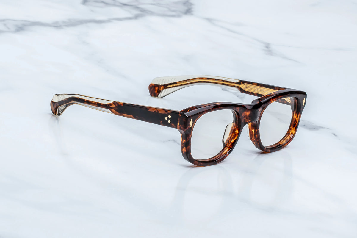 Three-quarter studio shot of the Jacques Marie Mage Amilcar RX Argyle frames. The perspective showcases the heavy 10mm profile depth and the elegant, streamlined curves of the frame face. The clear demo lenses highlight the structural thickness of the round rims, which taper smoothly into the custom double-laminated temple construction. Available at WINK Optometrists