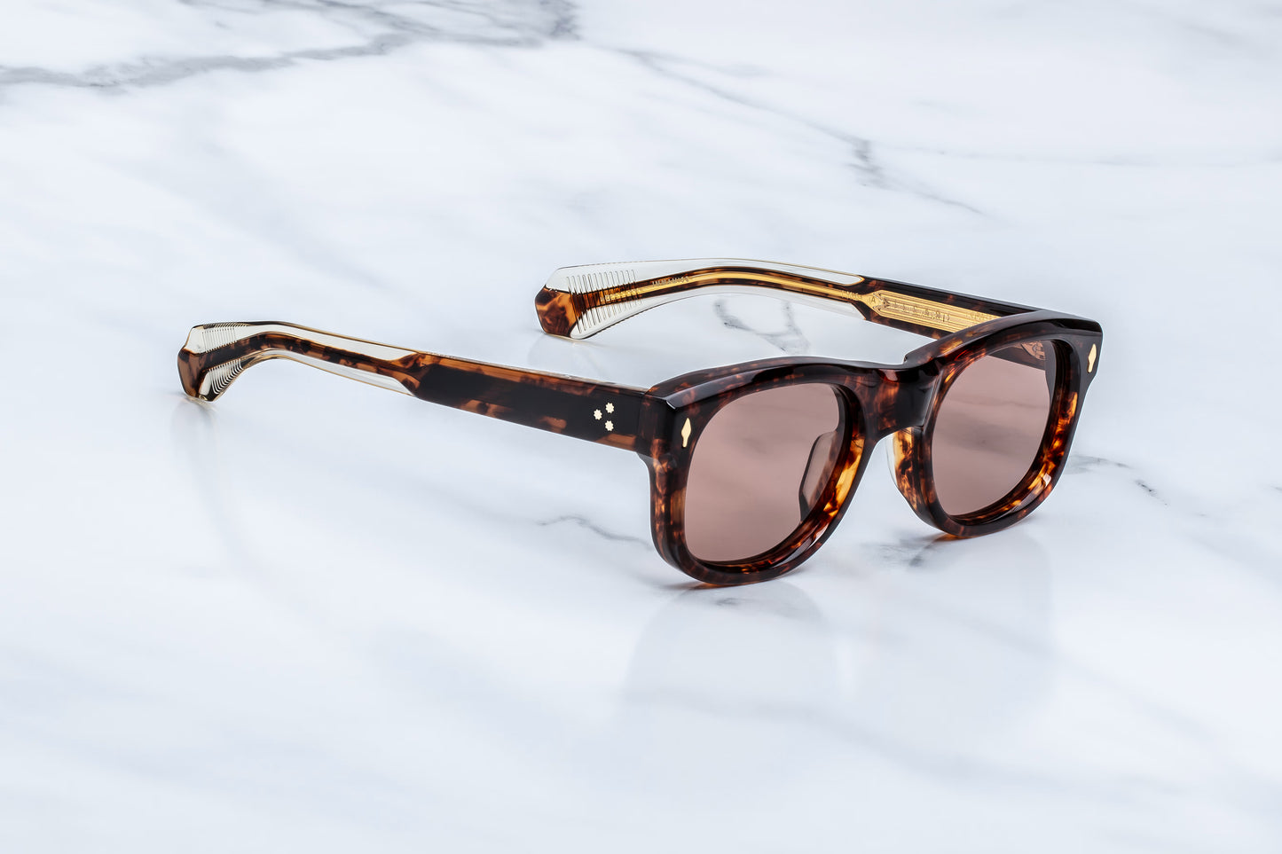 Three-quarter studio shot of the JMM Amilcar Argyle sunglasses, highlighting the substantial 10mm thick block frame, deeply recessed bronze lenses, and rich amber-brown tortoise shell tones