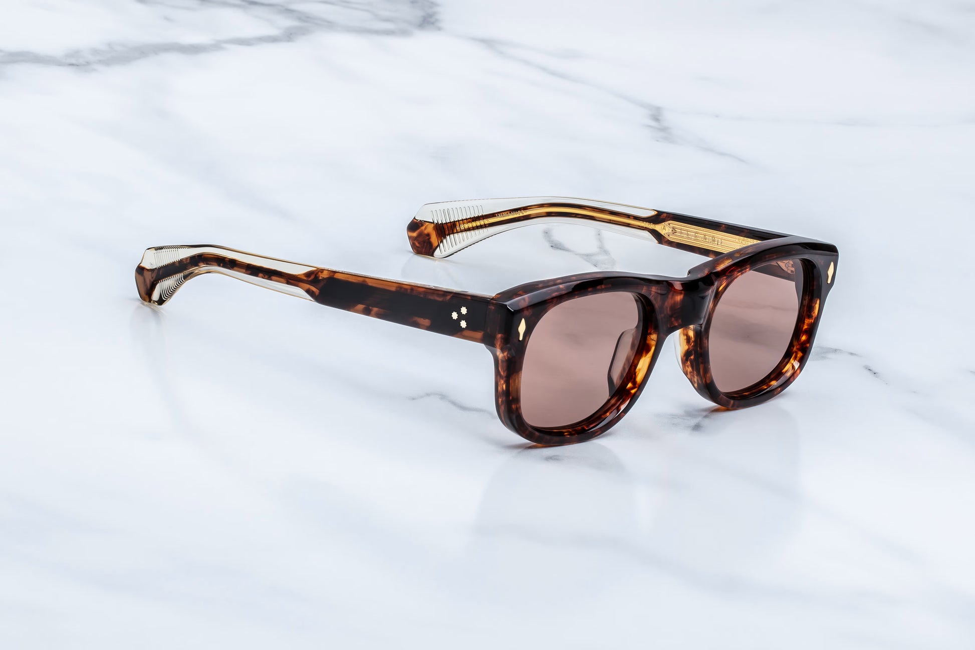 Three-quarter studio shot of the JMM Amilcar Argyle sunglasses, highlighting the substantial 10mm thick block frame, deeply recessed bronze lenses, and rich amber-brown tortoise shell tones