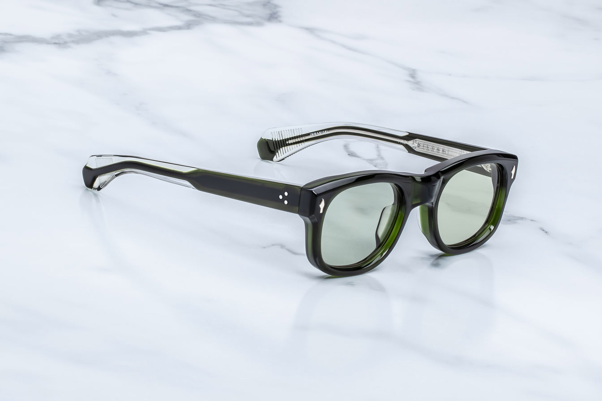 Three-quarter studio shot of the JMM Amilcar Borneo sunglasses, highlighting the substantial 10mm thick sculpted block frame, deeply recessed light bottle green lenses, and rich forest-green acetate tones.