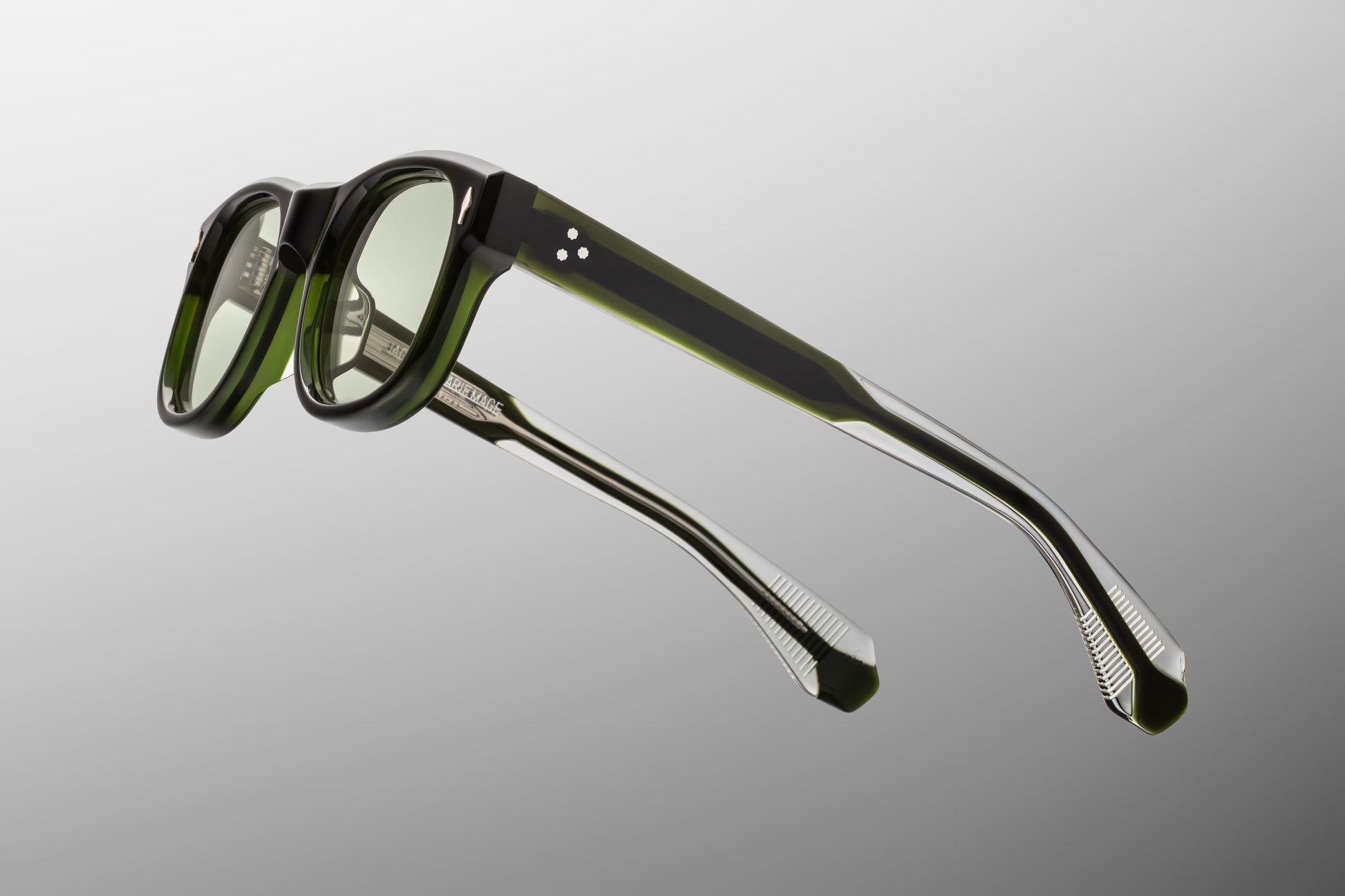 Side view of the JMM Amilcar sunglasses temple arm, showcasing the glossy green outer finish, silver spur-shaped rivet heads, and the silver palladium wirecore visible through the double-laminated construction.
