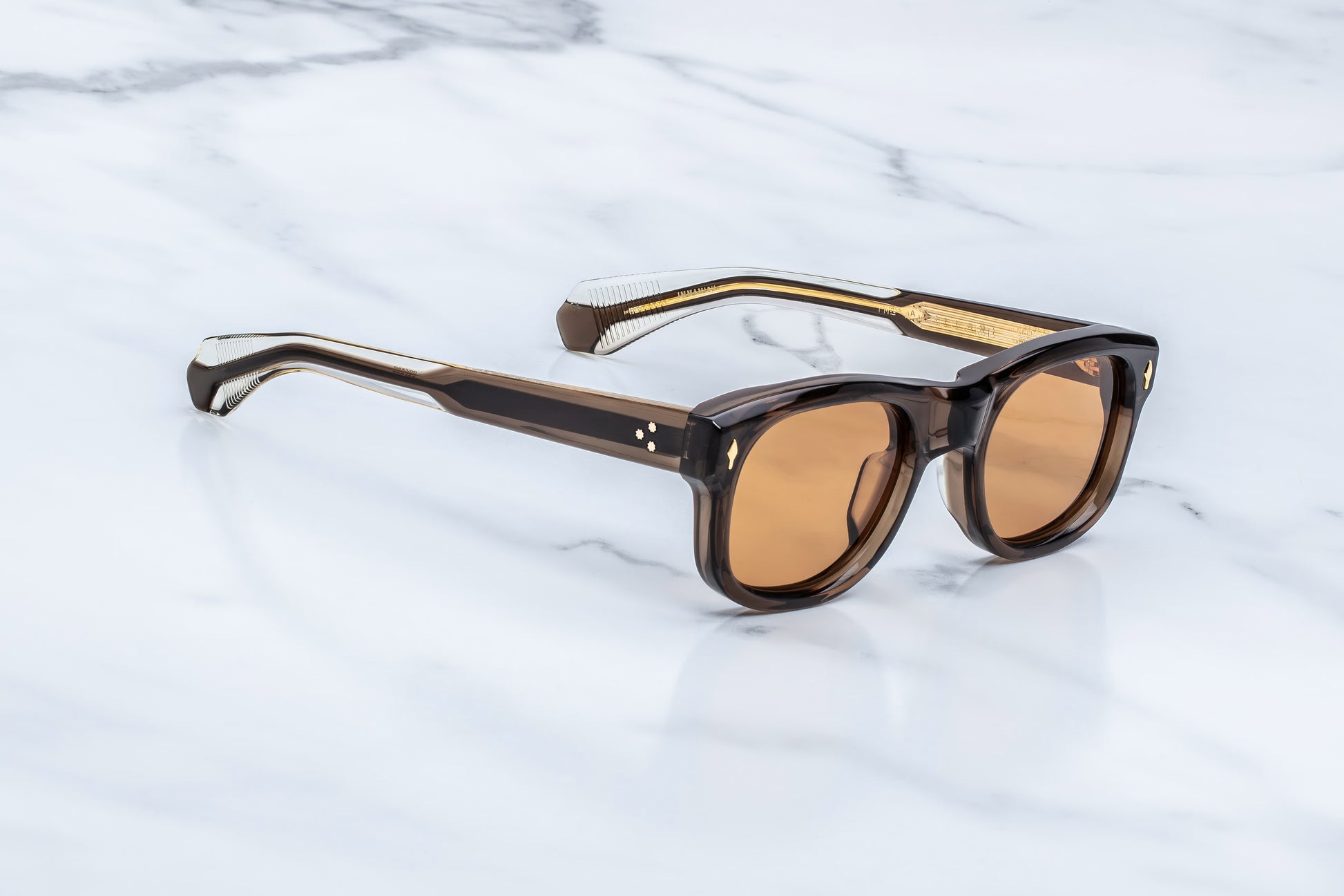 Three-quarter studio shot of the JMM Amilcar London sunglasses, highlighting the substantial 10mm thick block frame, deeply recessed orange lenses, and the warm, translucent brown acetate tones.