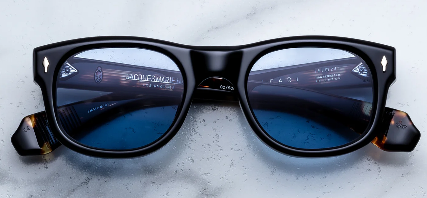 Front view of Jacques Marie Mage Amilcar sunglasses in Noir black acetate, showcasing classic round lenses with softly arched brows, a sleek metal top bar, and signature dark gold arrowhead pins