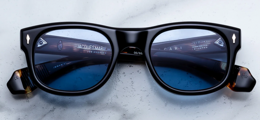 Front view of Jacques Marie Mage Amilcar sunglasses in Noir black acetate, showcasing classic round lenses with softly arched brows, a sleek metal top bar, and signature dark gold arrowhead pins