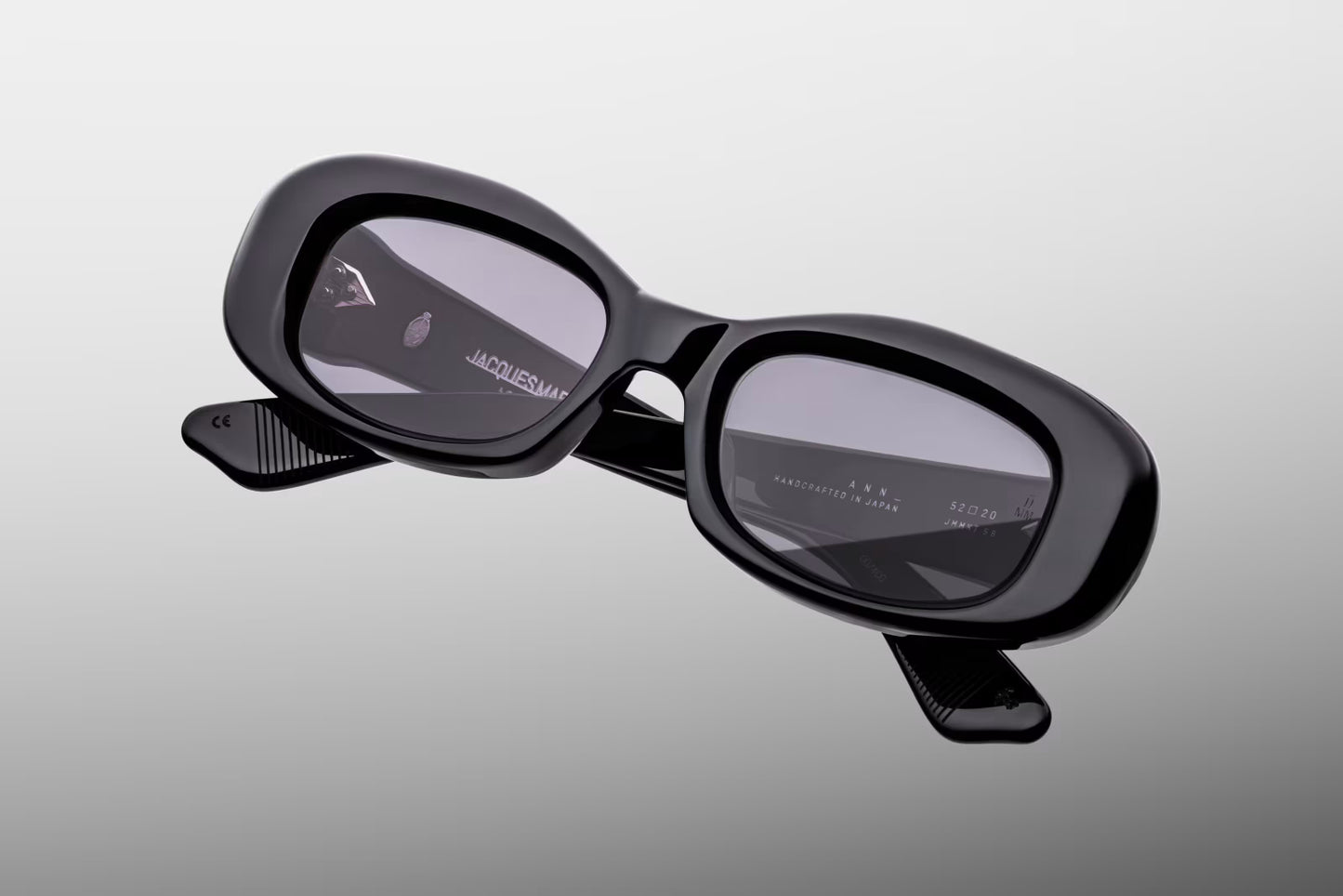 Close-up front detail of Jacques Marie Mage Ann Raven frame showing spur-shaped rivets, bevelled edges and polished black acetate
Macro front view of JMM Ann Raven sunglasses highlighting rectangular lens shape and charcoal tint