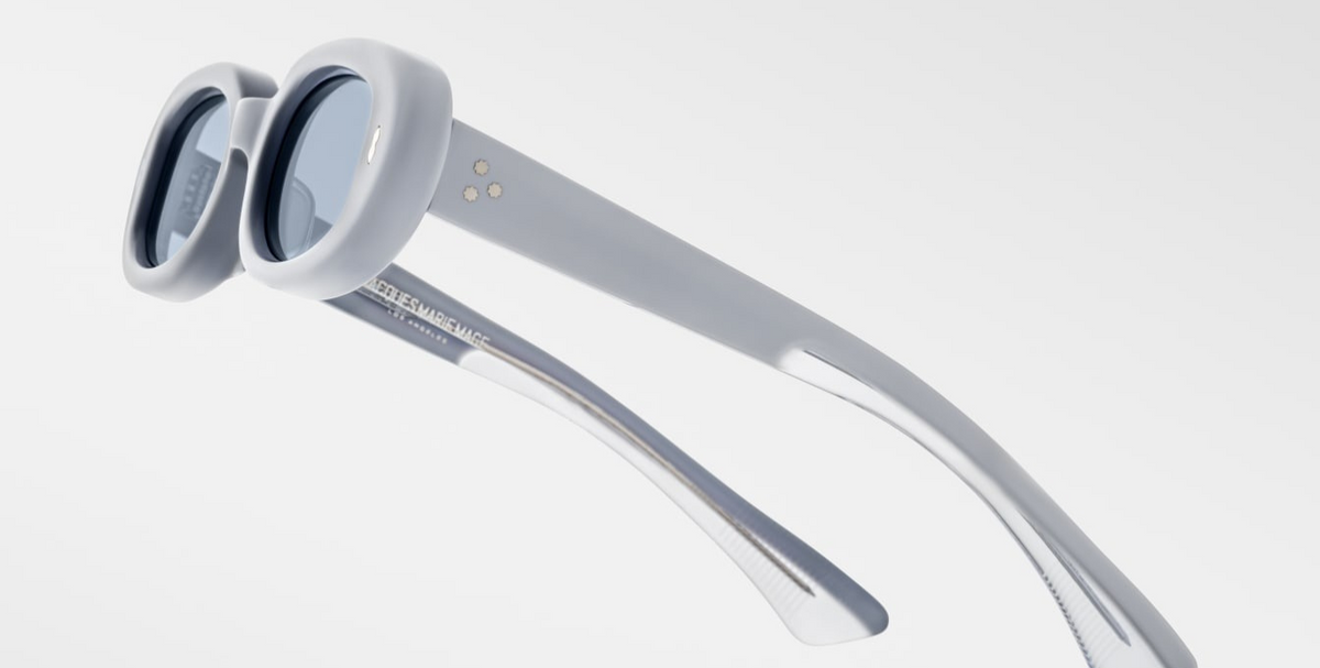 Close-up side of Jacques Marie Mage Besset Sky Suede temple—matte plant-based acetate, double‑laminated pastel blue interior, precious metal hardware, signature arrowhead pin, silver hairline‑engraved hinge.