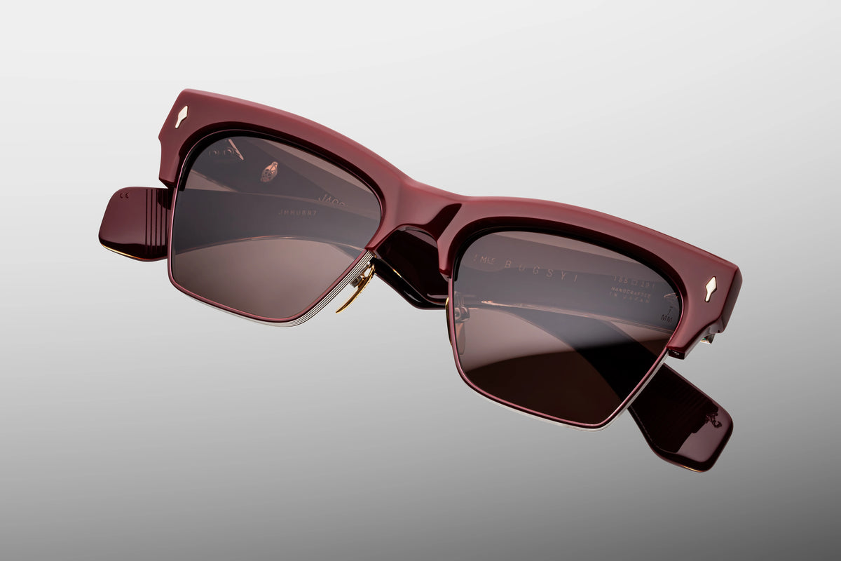 Extreme close-up of the front chassis on Jacques Marie Mage Bugsy Bordeaux Empire sunglasses. Captures the high-gloss luster of the red acetate brow, a flush silver palladium arrowhead pin, and the fine hairline engraving on the silver titanium rims.
