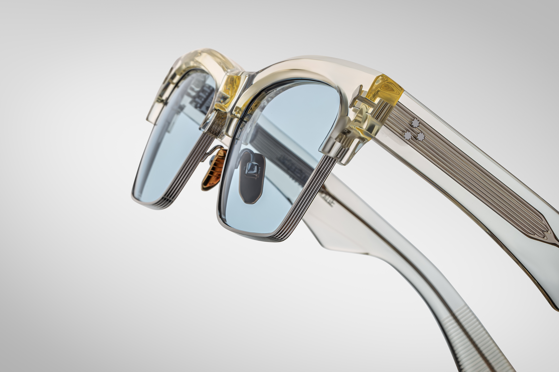 Close-up of Bugsy Brut temple featuring crystal‑clear cured acetate layered over concealed wirecore, silver arrow‑head pin accent, and logo‑engraved custom nose pad visible from side edge