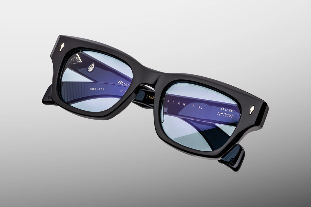  A macro close-up showcasing the front upper corner of the JMM Dealan 53 Obscure frame. The shot emphasizes the thick, bevelled edge of the 10mm hand-polished translucent navy-blue acetate, highlighting the signature sterling silver arrowhead pin resting completely flush against the dark blue backdrop