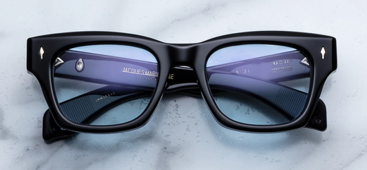 A front-facing product shot of Jacques Marie Mage Dealan 53 sunglasses in the Obscure colourway. The oversized, 10mm structured rectangular acetate frame with a subtle cat-eye flare is crafted from a rich, translucent deep ink-blue. Serene blue lenses are housed inside the substantial frame, flanked by iconic sterling silver arrowhead pins embedded horizontally on the upper outer corners.