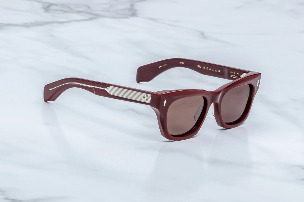 Three-quarter studio shot of the Jacques Marie Mage Dealan Bordeaux Empire sunglasses. The perspective highlights the heavy 10mm profile depth of the translucent cassis red acetate frame face and its sharp, sculpted lines. The rich ruby sunglass lenses catch the studio lighting, flowing smoothly into the substantial, double-laminated matching burgundy temples. Available at WINK Optometrists