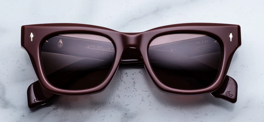  Front view of Jacques Marie Mage Dealan sunglasses in Bordeaux Empire. The frame displays a bold, 1960s-inspired rectangular silhouette featuring a subtle cat-eye lift and strong, confident proportions. The 10mm block acetate is a deep, polished cassis burgundy-red, housing striking ruby-tinted lenses. Signature sterling silver arrowhead front pins with custom hand-painted bordeaux epoxy enamel inlays accent the upper outer corners. Available at WINK Optometrists
