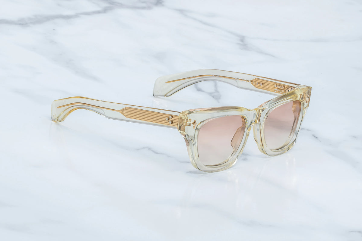 Three-quarter studio shot of the Jacques Marie Mage Dealan Halo photochromic sunglasses. The perspective highlights the heavy 10mm profile depth of the translucent champagne-beige acetate frame face and its sharp, sculpted lines. The photochromic brown gradient lenses show a soft transition, flowing smoothly into matching clear beige temples. Available at WINK Optometrists.