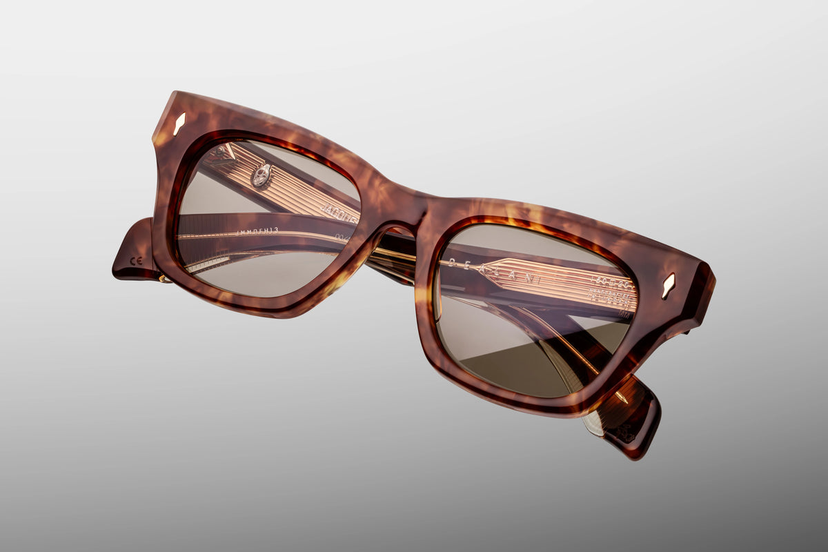 A macro close-up focusing on the front upper corner of the JMM Dealan 50/20 Honeycomb frame. The shot showcases the premium hand-polished edge of the compact 10mm thick acetate, emphasizing the depth of the translucent golden-amber sections next to a flush-embedded light gold arrowhead front pin.