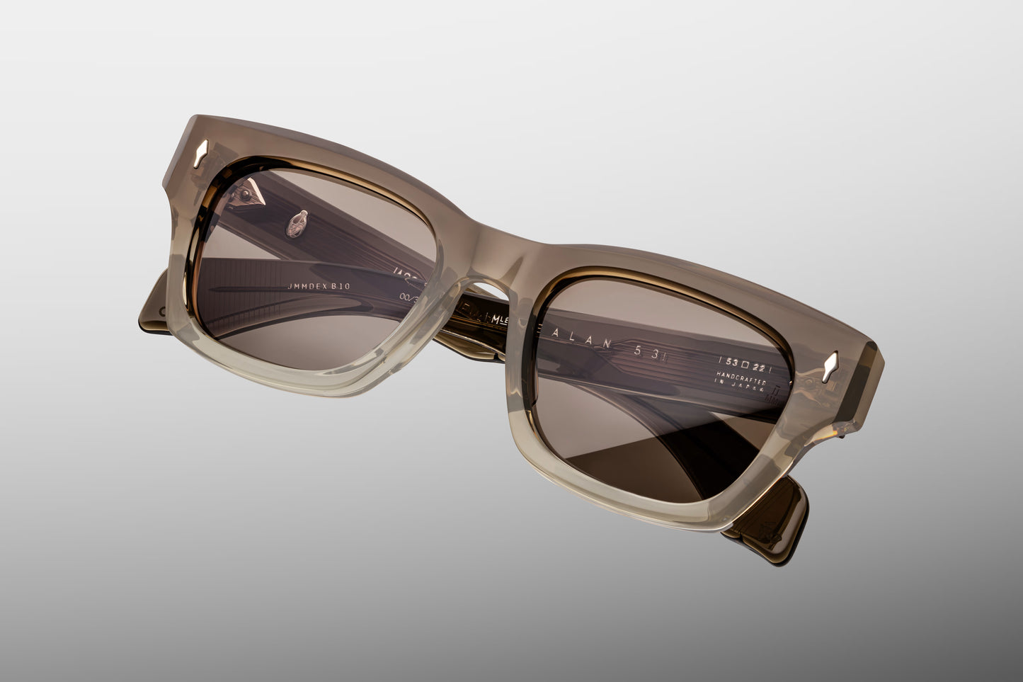 Top-down macro shot of Jacques Marie Mage Lescot sunglasses, highlighting the substantial 10mm thickness of the dark charcoal acetate frame and the precision-engineered silver metal hardware.