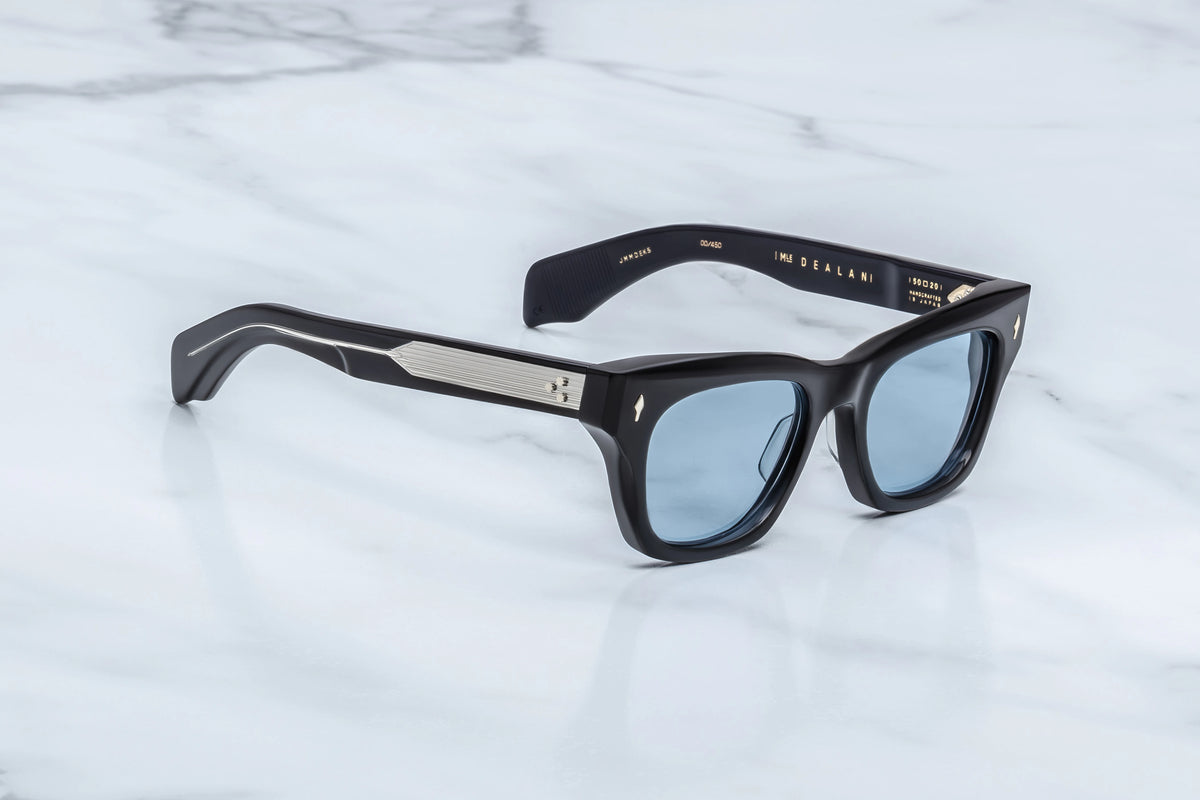 Three-quarter studio shot of the Jacques Marie Mage Dealan Obscure sunglasses. The angled view shows off the heavy 10mm profile depth of the translucent blue acetate rims and the sharp, sculpted lines of the frame face. The Serene Blue sunglass lenses catch the light, transitioning into custom double-laminated temples. Available at WINK Optometrists.