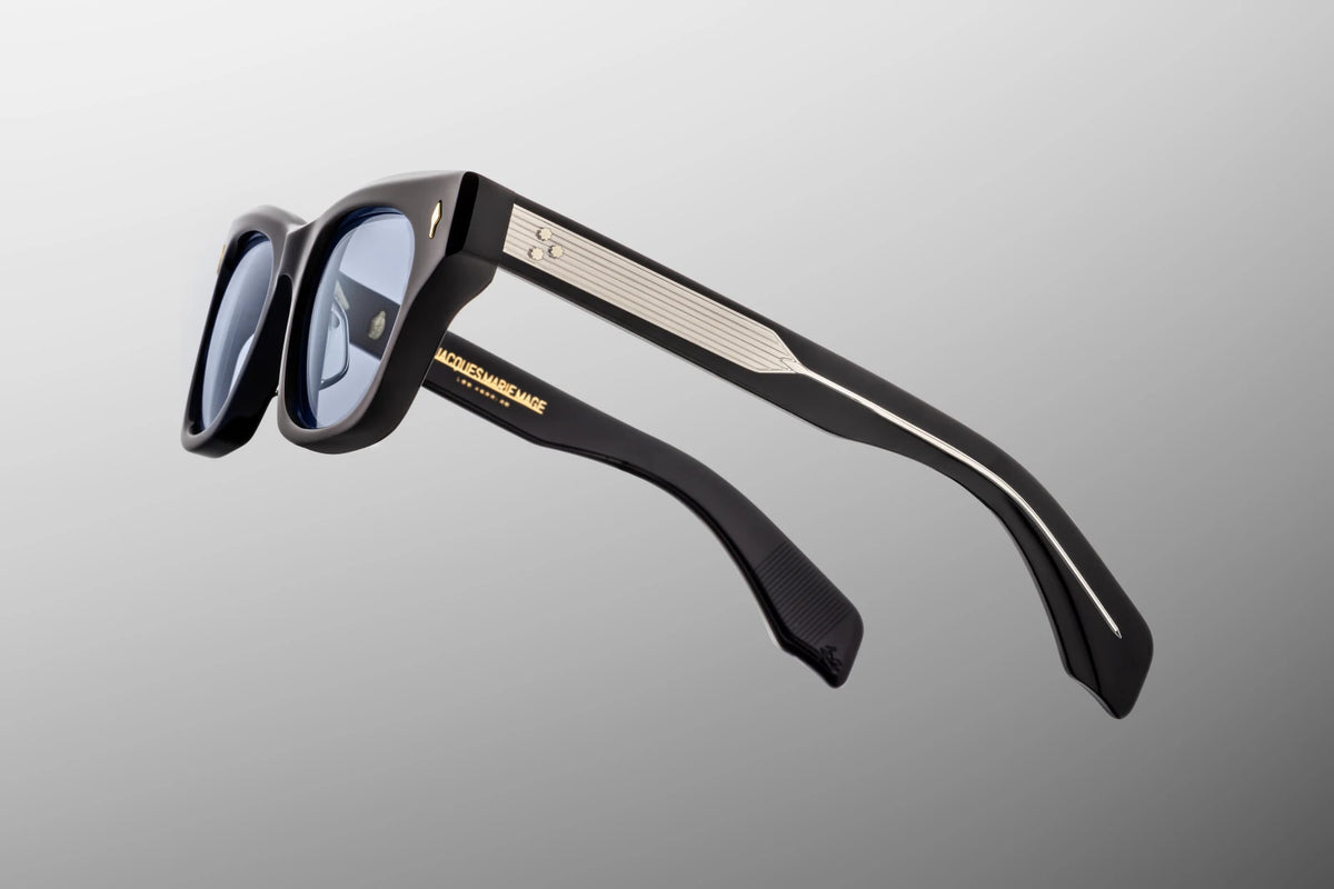 Side profile view of the Jacques Marie Mage Dealan in Obscure. The focus is on the thick, sculptural paddle temple arms crafted from custom double-laminated blue acetate. A dark gold tension-secured custom 7-barrel hinge elegantly anchors the side arms to the deep blue frame face. Available at WINK Optometrists.
