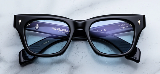 Front view of Jacques Marie Mage Dealan sunglasses in Obscure. The frame features a bold, '60s-inspired rectangular silhouette with a subtle cat-eye lift and strong, chunky volumes. The 10mm block acetate is a deep, moody translucent blue tone, accented by signature sterling silver arrowhead front pins at the upper outer corners. The frame houses rich, solid Serene Blue lenses. Available at WINK Optometrists.
