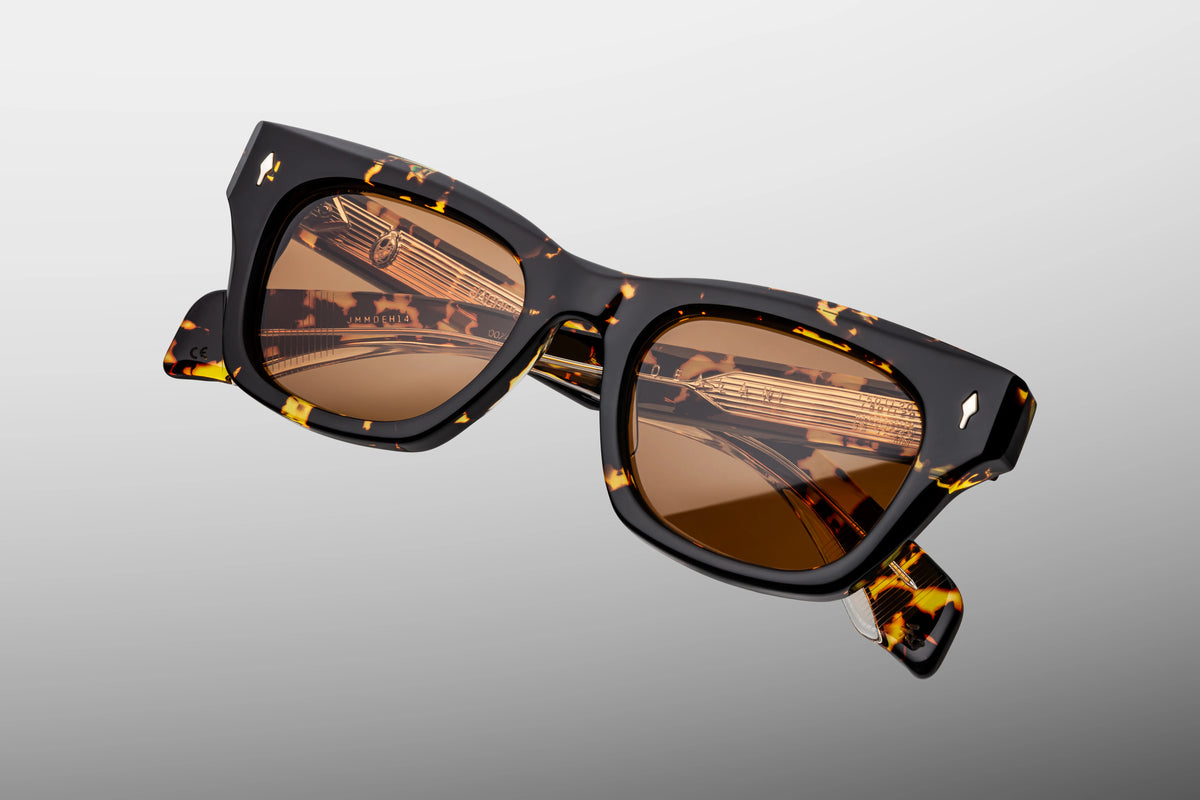  A macro close-up of the front upper corner of the JMM Dealan Tokyo frame. The image captures the thick 10mm hand-polished edge of the frame, showing the deep contrast of the dark brown and black tortoiseshell acetate next to a flush-embedded precious metal arrowhead pin.