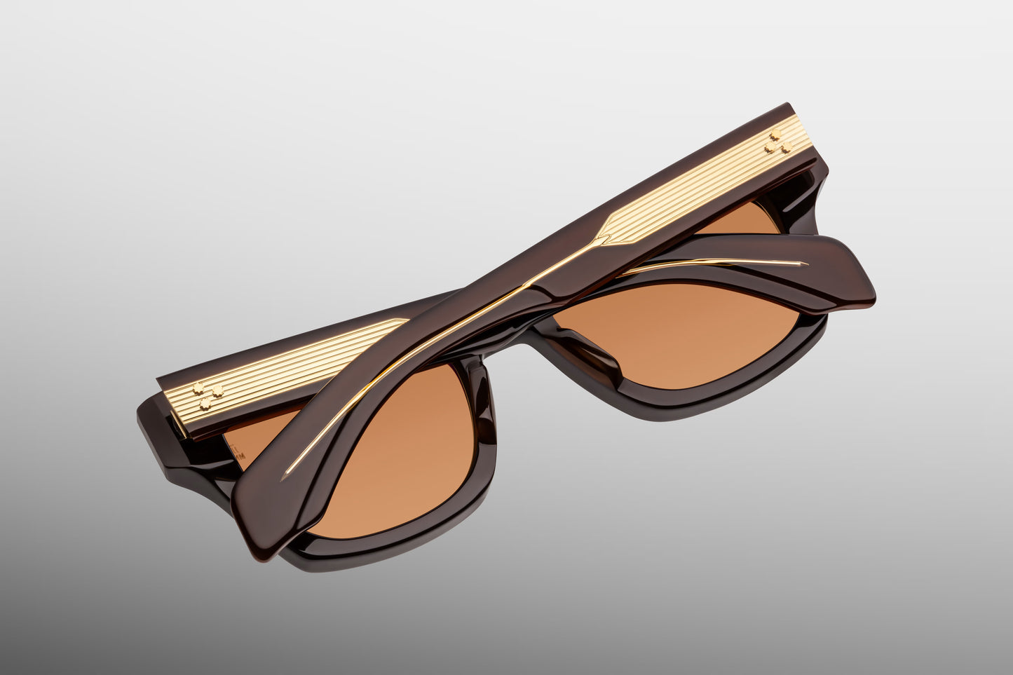 Close-up from the back of Jacques Marie Mage Dealan 53 Walnut sunglasses, showcasing the inner side-temple serial number stamping, the dark gold 7-barrel hinge, and the orange lenses.
