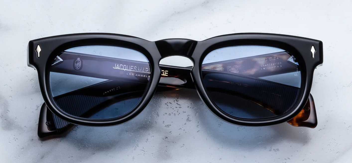 Front view of Jacques Marie Mage Pepper 10Y sunglasses in polished Noir black acetate, showing a round-oval 1960s-inspired frame with a classic keyhole bridge, Cerulean blue lenses, and sterling silver arrowhead pins