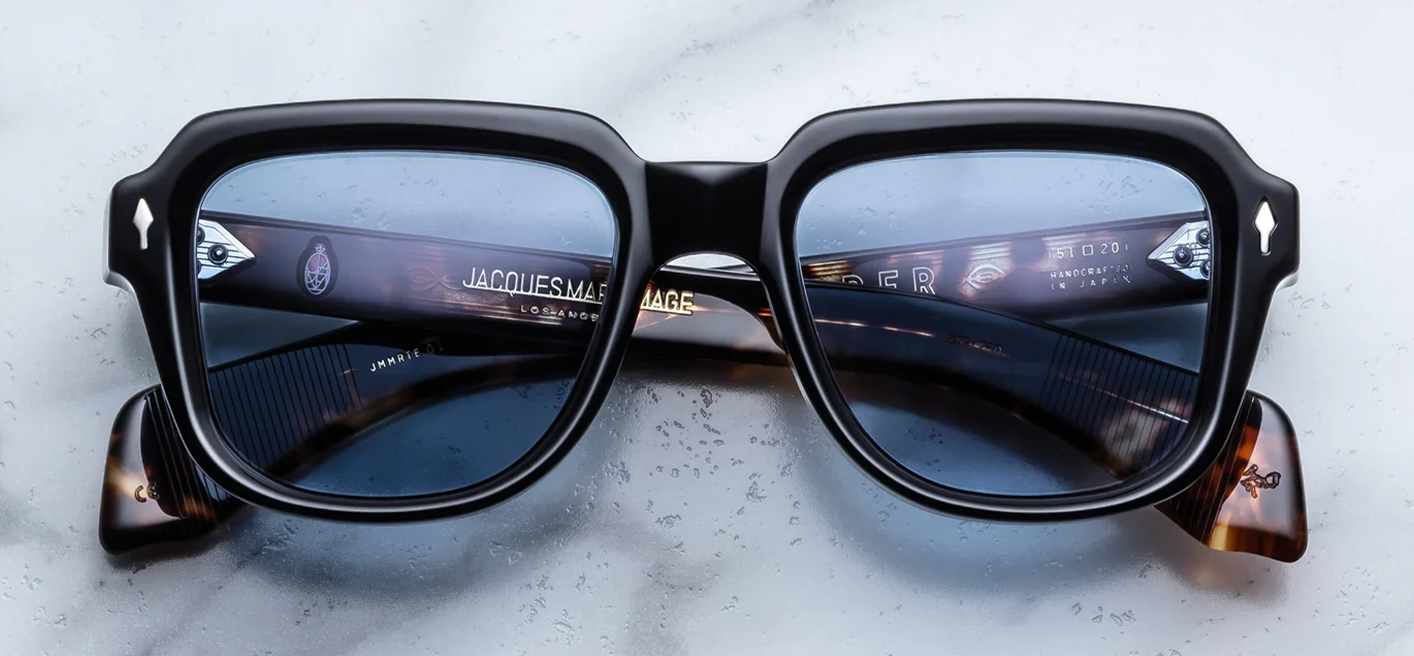 Front view of Jacques Marie Mage Taos 10Y sunglasses in polished Noir black acetate, showcasing a wide rectangular 1960s-inspired frame with Cerulean blue lenses and sterling silver arrowhead pins