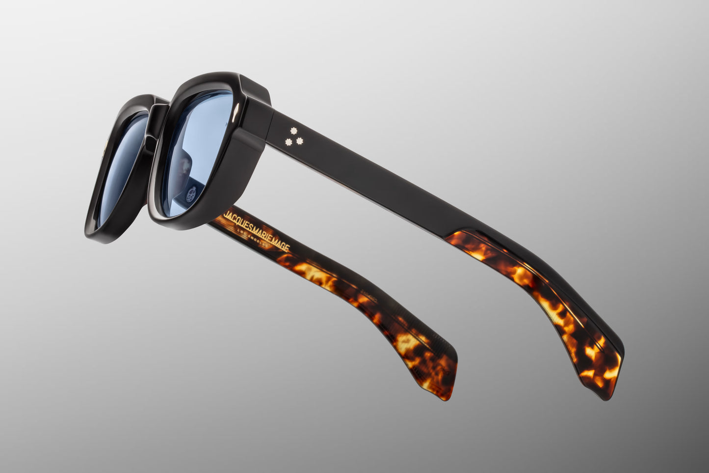 Side view of the JMM Taos 10Y sunglasses temple arm, showcasing the glossy black outer frame, rich tortoise shell inner lining, and spur-shaped palladium rivet heads.