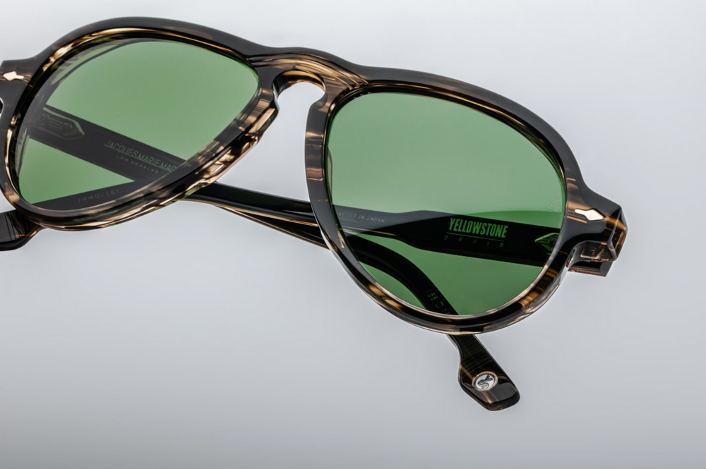 Angled downward view of Druid Lodgepole highlighting forest green polarized lenses with backside anti‑reflective treatment, 100% UV protection, and textured taupe tort acetate frame with metal embellishments.