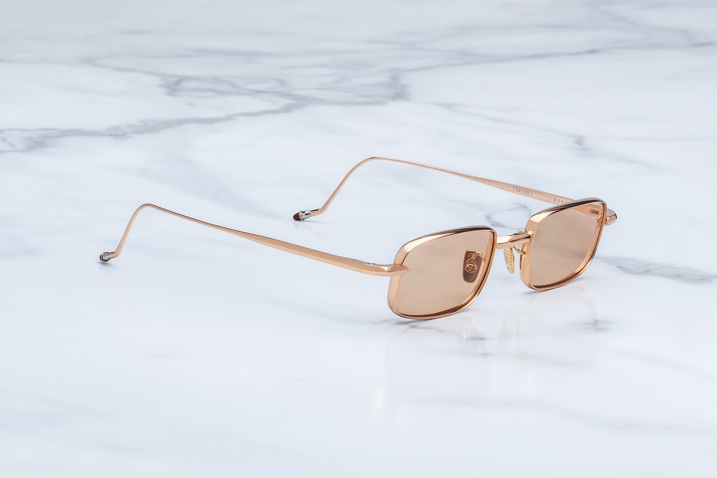  Three-quarter angled view of the JMM Dusk Sweetheart sunglasses, showcasing the slim rectangular shape, structural semilunar frame edges, and thin rose gold beta titanium build.