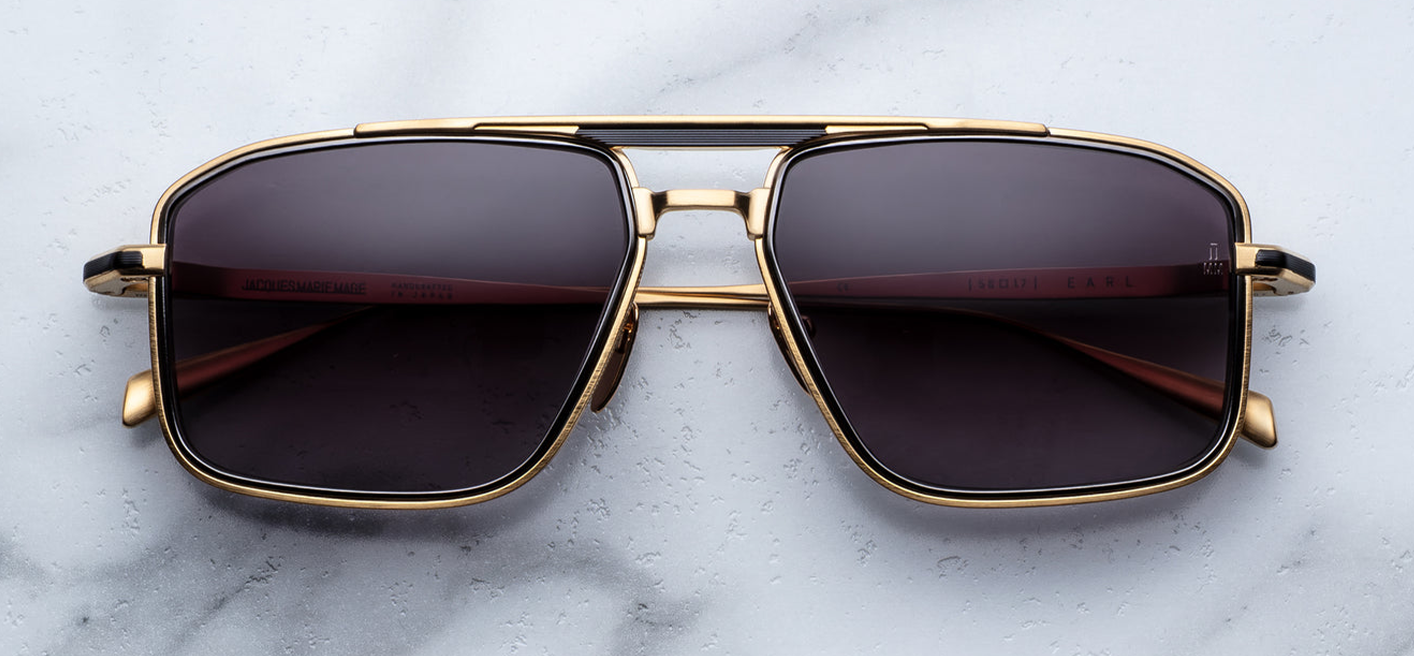 Front view of Jacques Marie Mage Earl CIA sunglasses: ‘70s-inspired titanium navigator frame in dark‑gold beta titanium with black eyerim inserts, jet-gradient CR‑39 lenses with backside AR, and Art Deco arrowhead embellishments