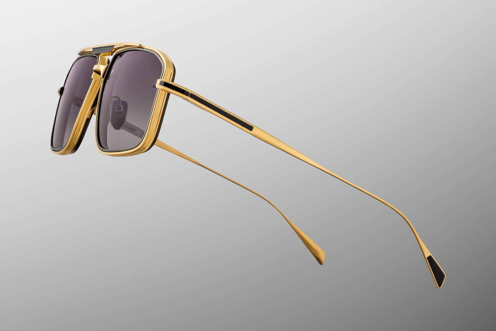 Side close-up of Earl CIA temple showing dark-gold beta titanium structure, custom arrowhead monoblock hinge, engraved logo nose pad, and smooth black acetate eyerim tip.