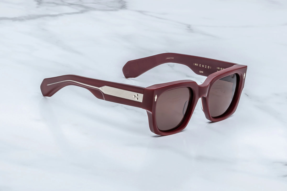 Three-quarter view of the Jacques Marie Mage Enzo Bordeaux Empire sunglasses. This angle highlights the immense architectural frame front volume, heavy blocky chassis, and thick temples that transition cleanly from the burgundy frame front.