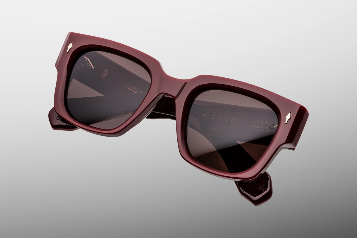 Extreme close-up of the front chassis on Jacques Marie Mage Enzo Bordeaux Empire sunglasses. Captures the high-gloss luster of the rich wine-red acetate, the smooth hand-polished square edges, and a flush-mounted sterling silver arrowhead pin.