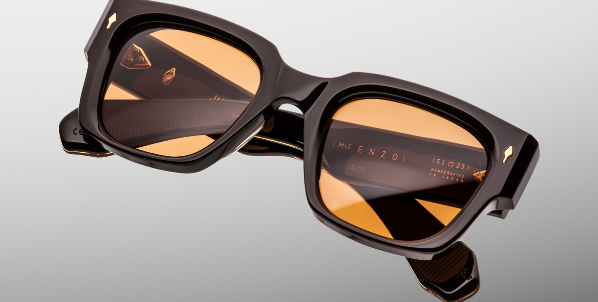 Close-up of the front of Jacques Marie Mage Enzo (Walnut) — detailed view of walnut-brown acetate texture, dark gold arrowhead pin, and vivid orange lenses with anti-reflective finish