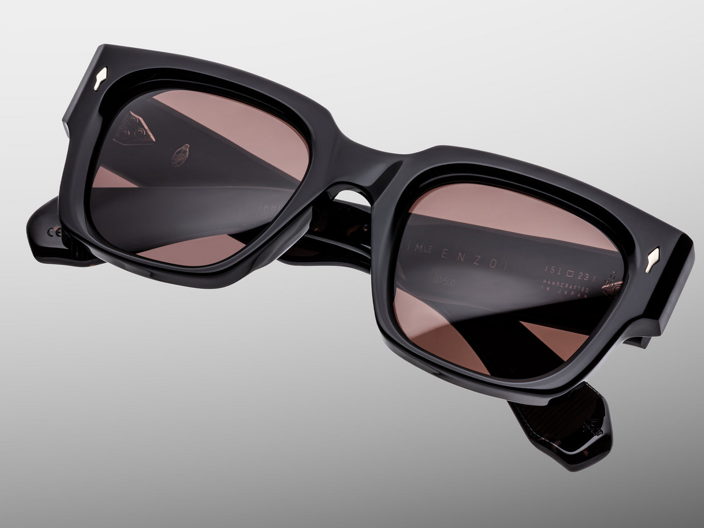 Close‑up front detail of Jacques Marie Mage Enzo (Willow) — textured black acetate brow‑line, sterling‑silver arrowhead front‑pin, and rich brown lenses with 100% UV protection