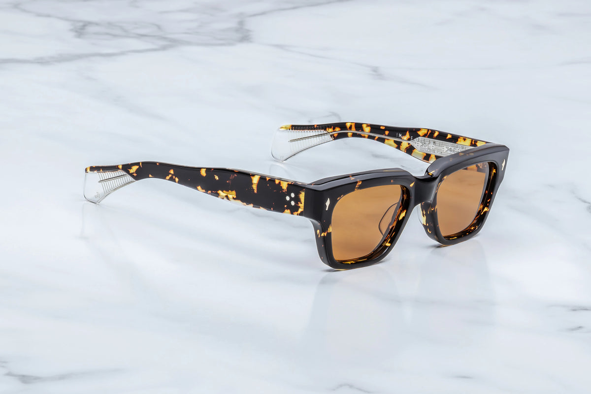 Side profile view of the Jacques Marie Mage Fellini Tokyo sunglasses. The thick, custom double-laminated acetate temple arms measure 150mm in length and extend straight back before tapering near the ears. The frame boasts a highly polished, glossy finish that accentuates the deep brown, black, and amber mottled pattern of the Havana exterior layer