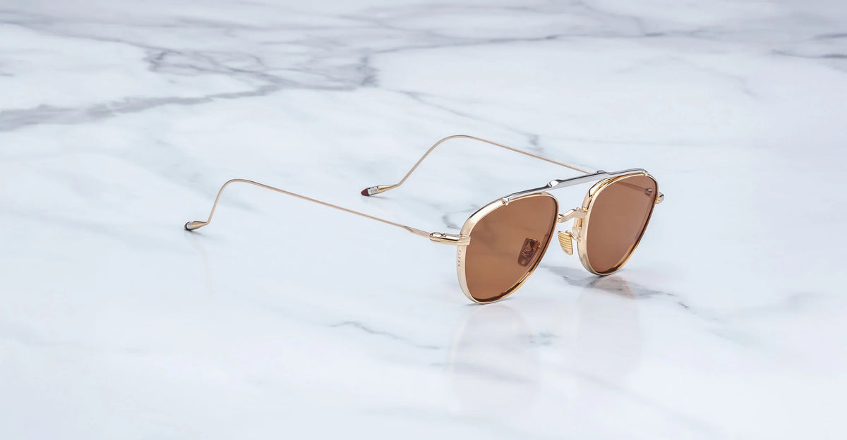 Three-quarter view of the Jacques Marie Mage Flynn Darjeeling sunglasses. This angle highlights the streamlined, dual-tone metal architecture of the gold and silver titanium chassis and the thin wire temples bridging into the sleek frame front.