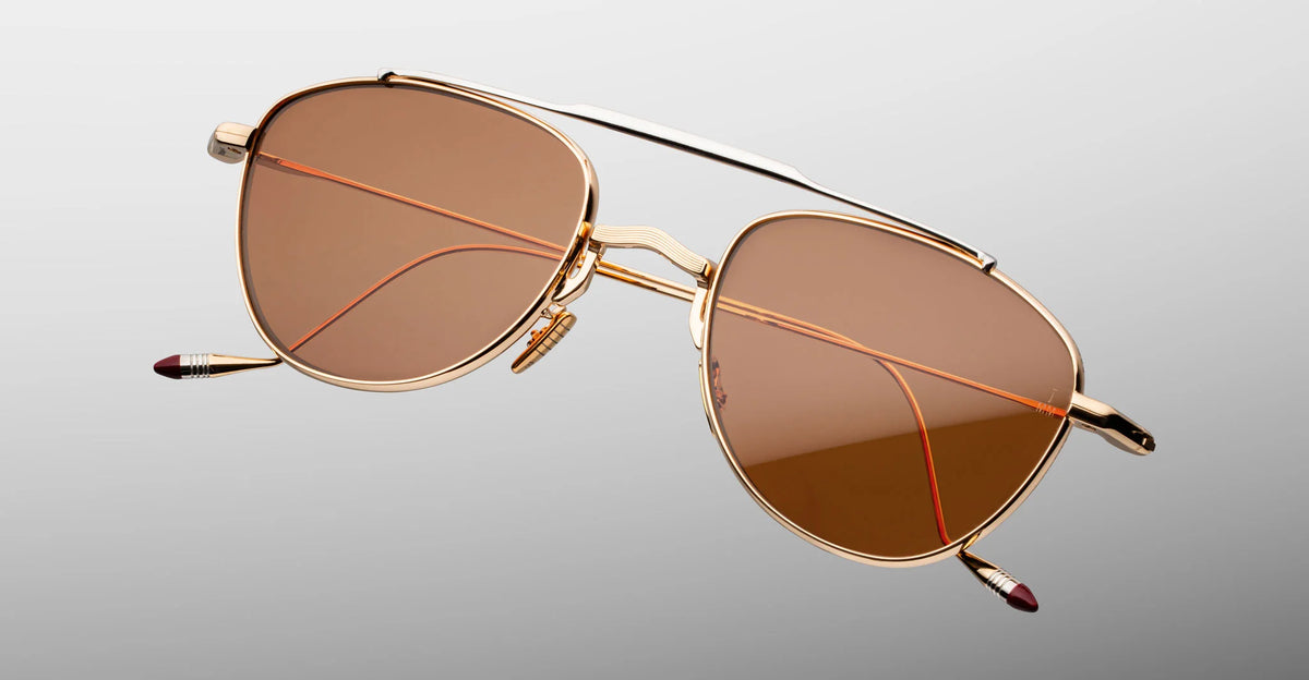 Extreme close-up of the front bridge on Jacques Marie Mage Flynn Darjeeling sunglasses. Captures the fine craftsmanship of the polished light gold nose bridge, custom micro-engraved titanium nose pads, and the polished silver palladium top bar.