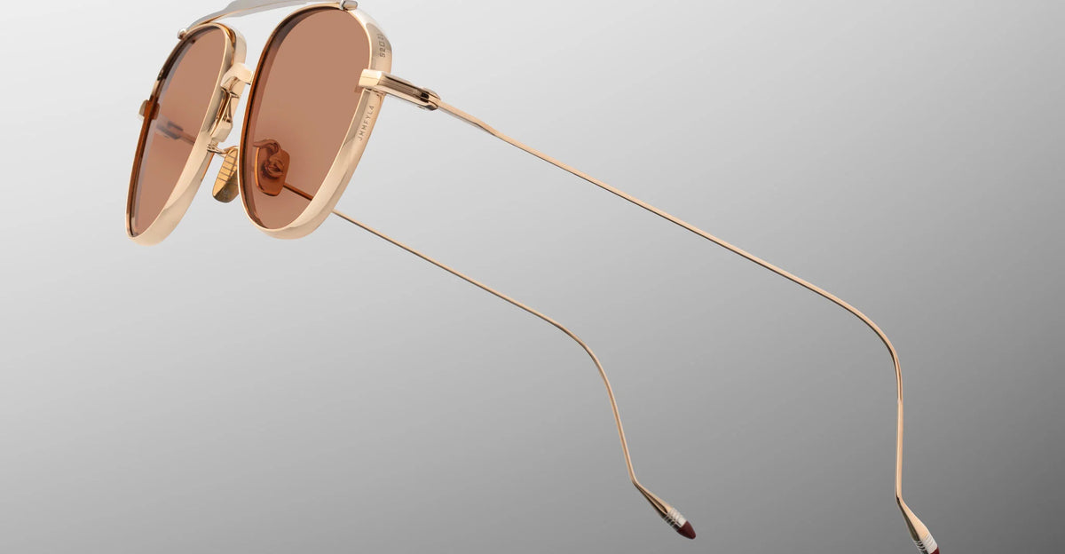 Macro shot of the temple arm on Jacques Marie Mage Flynn Darjeeling sunglasses, emphasizing the sleek transition from the light-gold tension-secured custom block hinge into the fine wire temple accented by hand-painted burgundy epoxy tips.