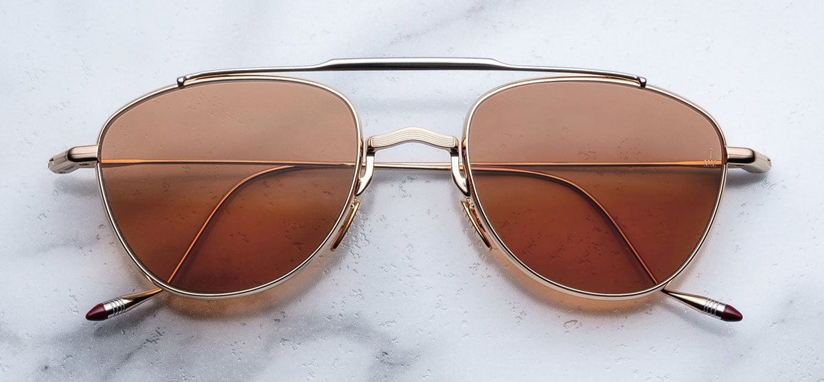  Front view of Jacques Marie Mage Flynn Darjeeling sunglasses. Displays a compact, lightweight 100% beta titanium pilot aviator frame with a polished light gold double-bridge design, a contrasting silver palladium top bar, and warm brown-green Darjeeling lenses.