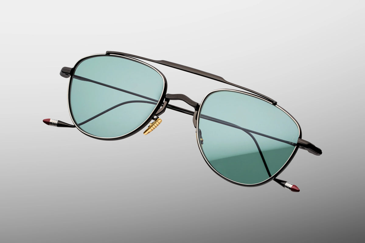 Extreme close-up of the front chassis on Jacques Marie Mage Flynn Paon sunglasses. Captures the high-contrast craftsmanship of the polished black nose bridge, custom gold titanium nose pads, and the polished silver palladium lunar-edged eye rims.