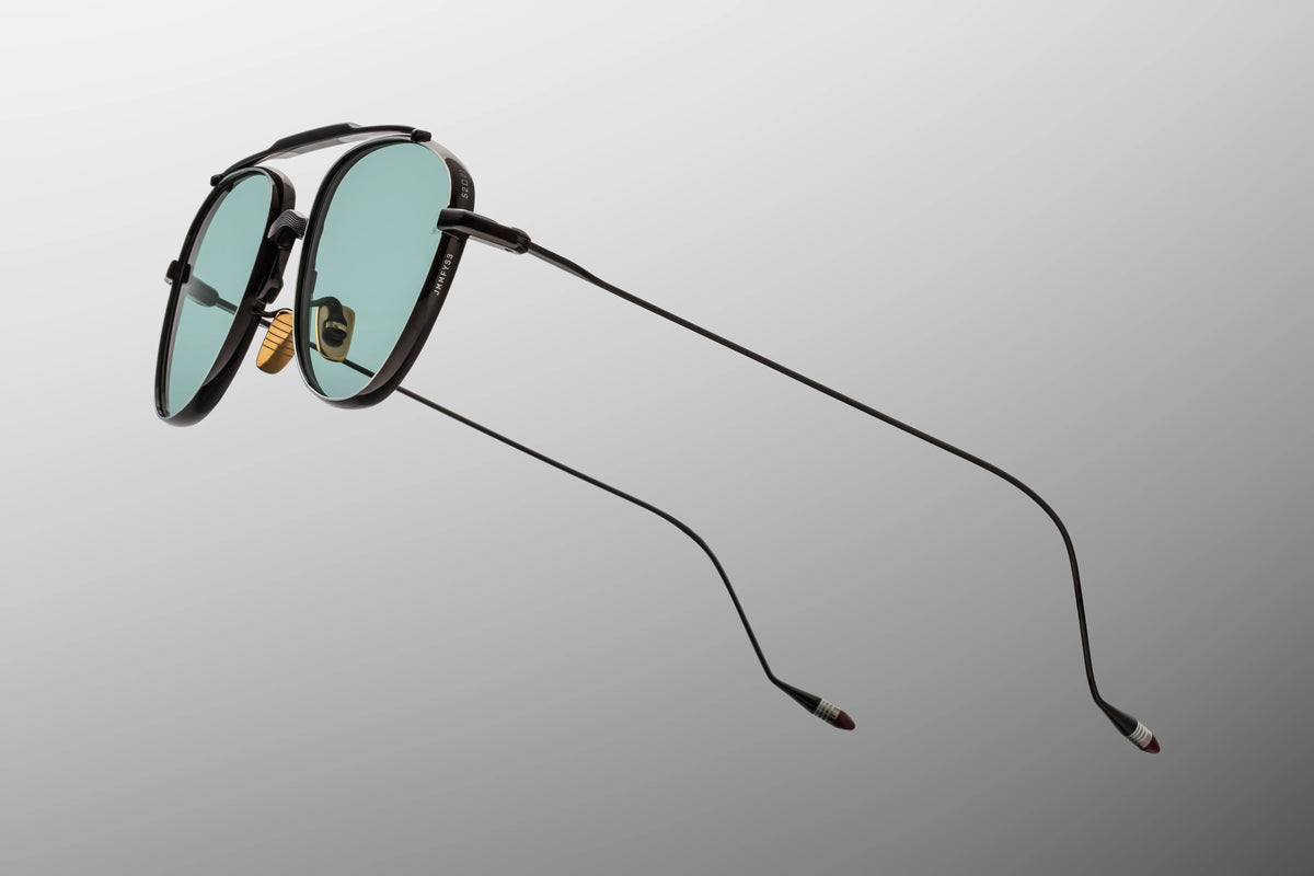 Macro shot of the temple arm on Jacques Marie Mage Flynn Paon sunglasses, emphasizing the sleek transition from the black block hinge into the fine wire temple accented by silver palladium and hand-painted burgundy epoxy tips.