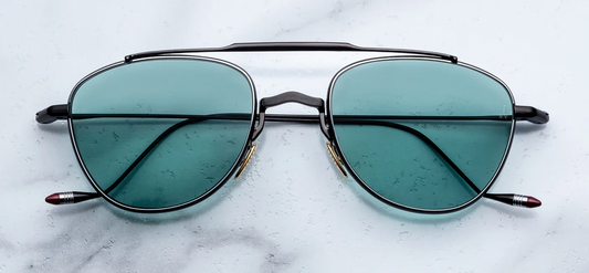 Front view of Jacques Marie Mage Flynn Paon sunglasses. Displays a compact, lightweight 100% beta titanium pilot aviator frame with a polished black double bridge, contrasting silver palladium eye rims, and vibrant turquoise solid-tint lenses.