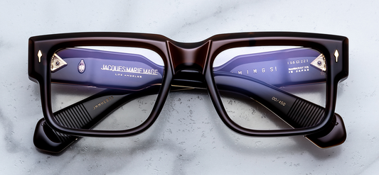 Front view of Jacques Marie Mage Hemmings Café RX optical glasses. Features a bold, boxy 10mm block acetate frame in deep espresso brown, fitted with clear demonstration lenses and signature gold arrowhead front pins.