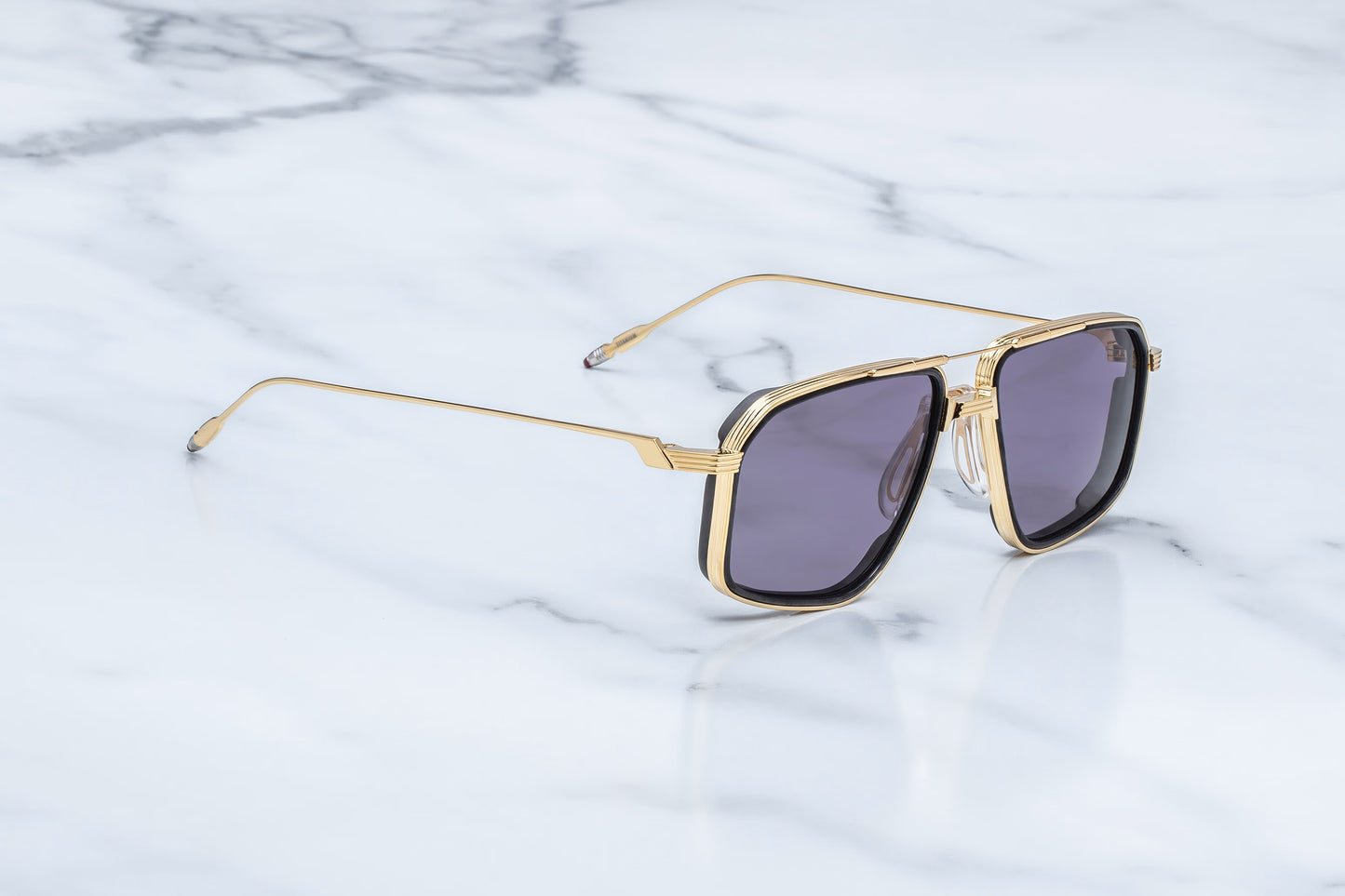 Three-quarter studio shot of the JMM Jagger Ebony sunglasses, highlighting the sculptural Art Deco-inspired double bridge, structural brow bar, and layered titanium eye-rims.