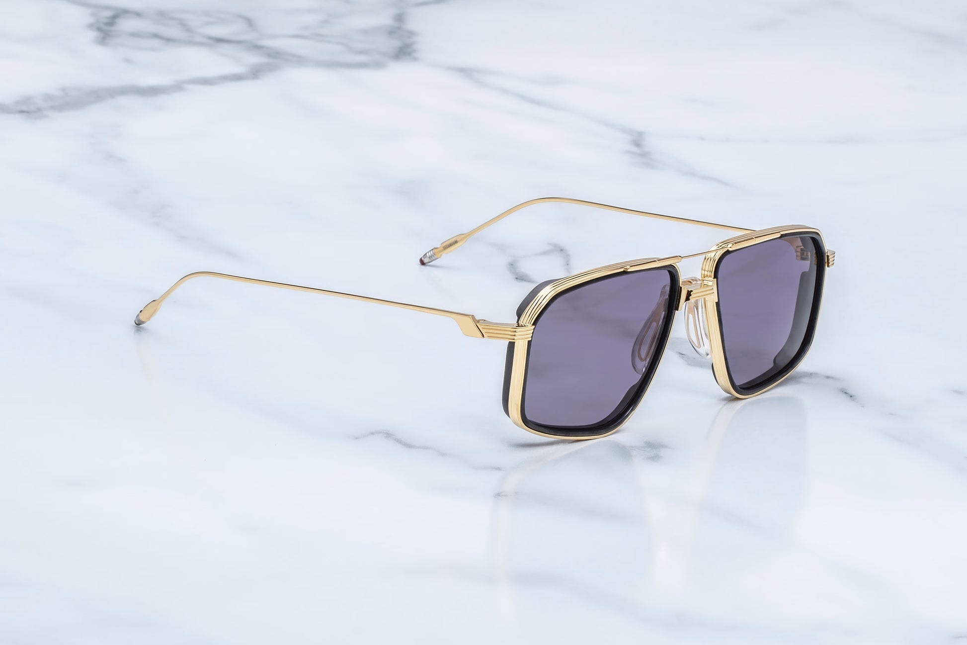 Three-quarter studio shot of the JMM Jagger Ebony sunglasses, highlighting the sculptural Art Deco-inspired double bridge, structural brow bar, and layered titanium eye-rims.